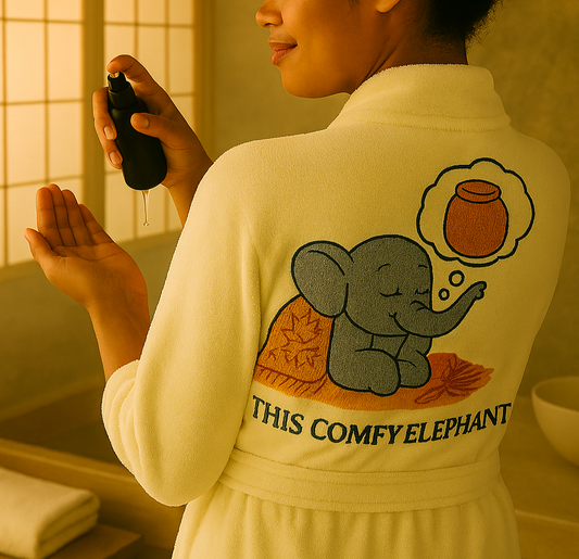 Woman in a 'This Comfy Elephant' robe applying lotion in a bathroom.