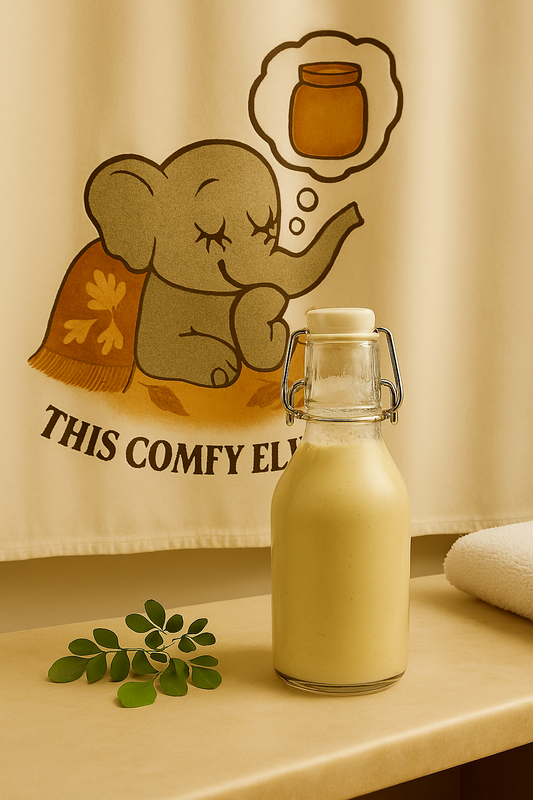 Glass bottle of Bath milk on a surface with a cartoon elephant and text towel in the background.